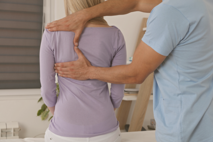 Physiotherapist with hands on woman patient's shoulder blade