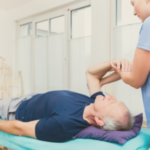 Older man lying down doing exercises for shoulder with physiotherapist