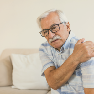 Older man holding shoulder in pain sitting on sofa